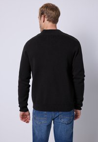 Svart stickad tröja med långa ärmar och rund halsringning, kombinerad med blå denimjeans med en klassisk femficksdesign.