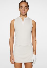 Ärmlös golfklänning i ljusbeige, med hög halsringning och dragkedja. Slätt tyg med figursydd midja och detalj i form av golfhandske.