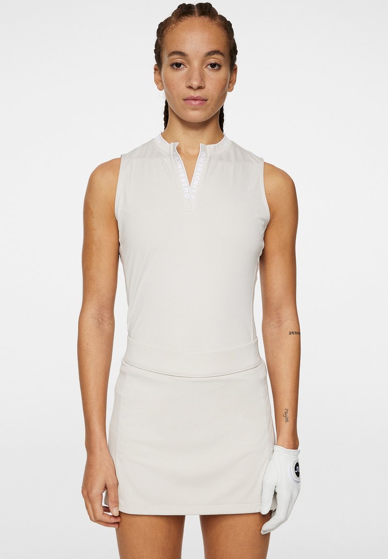 Ärmlös golfklänning i ljusbeige, med hög halsringning och dragkedja. Slätt tyg med figursydd midja och detalj i form av golfhandske.