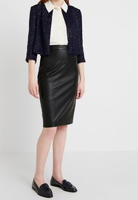 Námořnická tweedová zkrácená bunda přes bílou košilovou blůzu, spárovaná s úzkou černou koženou tužkovou sukní a černými mokasíny.