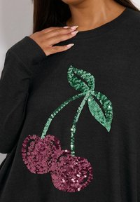 Czarna koszula z długim rękawem z grafiką wiśni w różowych i zielonych cekinach, o gładkiej fakturze i okrągłym dekolcie.