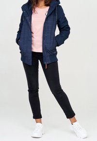 Marinblå hooded jacka med randig design, en rosa skjorta med en pingvin grafik, svarta tajta jeans och vita sneakers.