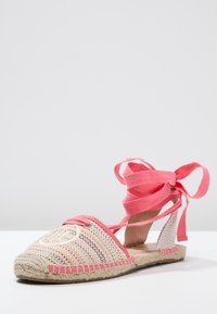 Espadrilles rosas y beige con parte superior de lona trenzada, punta redonda y cintas de lazo. Suela de yute con costura decorativa a lo largo del borde.