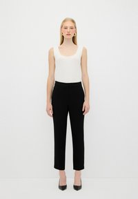 Bílý rypsový top a černé přiléhavé kalhoty se střihaným designem, rovnými nohavicemi a hladkým povrchem. Černé špičaté podpatky doplňují outfit.