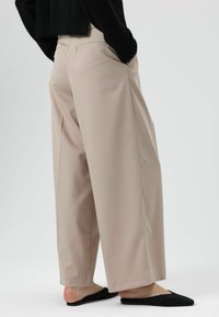 Beige wijde broek met gladde textuur, hoge taille en zijzakken, gecombineerd met zwarte instapschoenen.