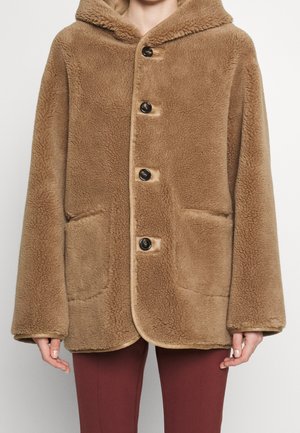 Brown hooded faux shearling coat with front buttons and two pockets, worn over maroon pants.