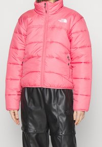 Giacca a vento rosa con cuciture orizzontali e colletto alto. Presenta tasche laterali con zip. Abbinata a pantaloni in finta pelle nera.