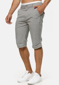 Gray and white checkered shorts with a button closure, side pockets, and folded hems. Worn with white sneakers.