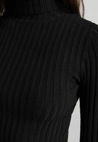 Svart ribbad turtlenecktröja med en åtsittande design, texturerad tyg och långa ärmar med vertikala ränder.