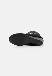 Botte de cheville en suede noir avec un bout rond, une semelle texturée et un détail de boucle en argent sur le côté. Talon plat pour le confort.