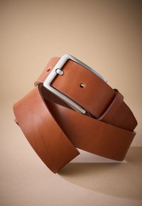 Ceinture en cuir marron avec une boucle en métal argenté. Texture lisse, design large, avec des trous perforés pour l'ajustement, présentée en position enroulée.