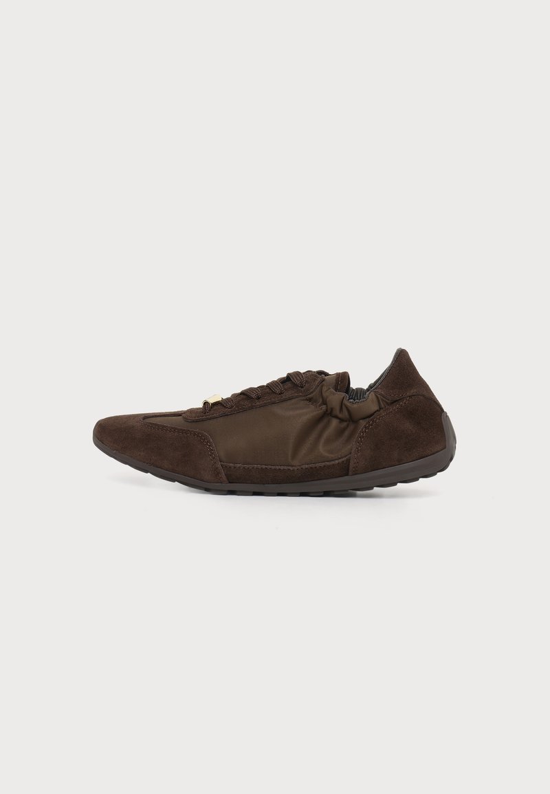 Chaussure casual basse marron avec fermeture à lacets à l’avant, panneaux en suède et tissu, et une semelle flexible sur un fond clair uni.
