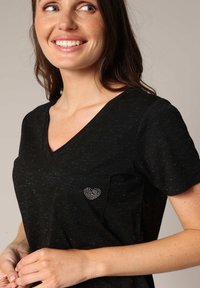 T-shirt noir à col en V avec une texture marbrée et un ornement en strass en forme de cœur argenté sur la poche gauche.