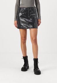 Zwarte glinsterende mini-rok met een aansluitend design en riemlussen, gecombineerd met hoge zwarte veterlaarzen. Glad, glanzend oppervlak.