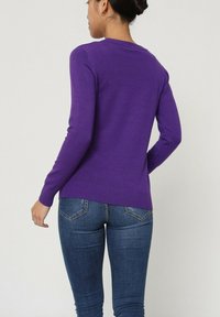 Pull en maille violet à manches longues et à ourlet côtelé. Associé à un jean en denim bleu foncé, doté d'un design à cinq poches et d'une légère élasticité.