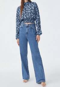 Haut court noir et bleu à imprimé floral avec taille élastique, assorti à un jean large à taille haute bleu clair et des sandales blanches à bout ouvert.
