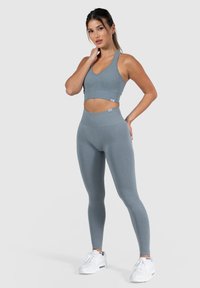 Grijze sportset bestaande uit een ribgebreide crop top en high-waisted leggings. Gemaakt van rekbaar materiaal met een gladde textuur, gecombineerd met witte sneakers.