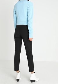 Lichtblauwe trui met geribde manchetten, zwarte strakke broek en witte enkellaarsjes met een spitse neus en een gestructureerde afwerking.