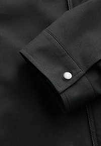 Črno tekstilno etui z srebrnim zadrgalnim gumbom. Ponaša se z teksturirano tkanino in vidnim šivanjem ob manšeti in šivu.