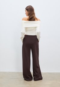 Weißes, geripptes, schulterfreies Oberteil mit langen Ärmeln, kombiniert mit weit geschnittenen braunen Hosen. Glatte Textur, lockere Passform, minimalistisches Design.