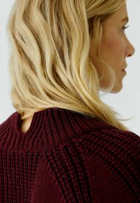 Burgundy knit sweater with textured stitching, high ribbed collar, and open back detail, showcasing a soft and warm fabric.