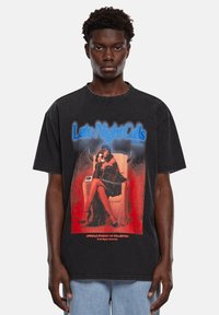 Schwarz oversized T-Shirt mit grafischem Druck einer sitzenden Figur in einem Kleid, mit dem Text "Late Night Calls" in blauen und roten Akzenten.