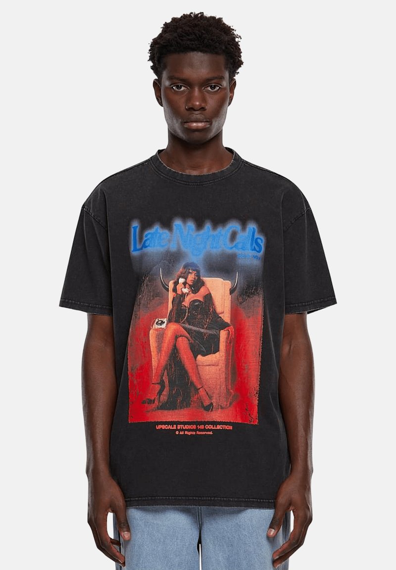 Schwarz oversized T-Shirt mit grafischem Druck einer sitzenden Figur in einem Kleid, mit dem Text "Late Night Calls" in blauen und roten Akzenten.