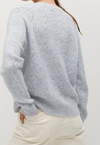 Pull en maille gris clair avec un motif en chevrons, des poignets et un ourlet côtelés. Texture douce et coupe décontractée avec un col rond.