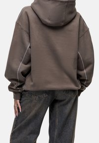 Ruskea ylipitkä huppari, jossa on nyörisäädettävä huppu, kontrastina valkoiset saumat ja muhkeat hihat. Yhdistetty tummiin farkkuihin.