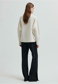 Maglione grigio chiaro oversize con spalle cadenti, abbinato a pantaloni neri a gamba larga con fessure laterali, creando una silhouette rilassata.