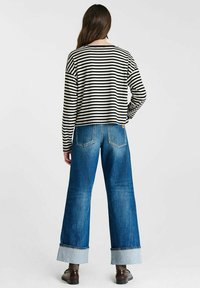 Zwart-wit gestreepte lange mouwen top, gecombineerd met een wijdvallende blauwe spijkerbroek met omgeslagen zoom en vijf zakken.