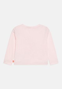 Chemise à manches longues en coton rose clair, avec un col rond et une petite étiquette décorative sur l'ourlet gauche. Texture lisse.