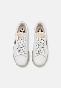White sneakers with a smooth leather surface, featuring patterned laces with text and hearts, and an inner sole design of a cartoon character.