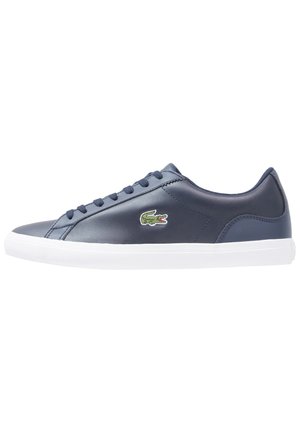 Navy blue low-top sneaker with white sole, lace-up front, and green crocodile logo on the side.