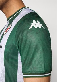 Grønn og hvitstripet sportsjersey med teksturert stoff, korte ermer, ribbestrikket hals, Kappa-logo på skulderen og et merke med en stjerne.
