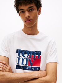 Witte katoenen t-shirt met een kleurrijke logo-afdruk die rode, blauwe en witte elementen bevat, ronde halslijn en korte mouwen.