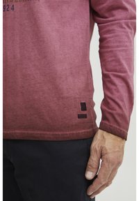 Piros ombré hosszú ujjú póló puha anyagból, enyhén texturált felülettel. Jellemzője egy logóhímzés és egy öltött szegély a alján.