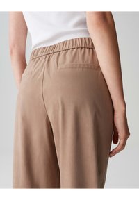 Beige, lockere Hose mit elastischem Bund und einer Gesäßtasche. Der Stoff wirkt weich mit einer glatten Textur.