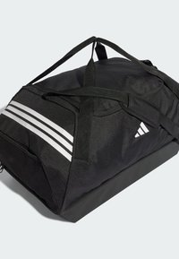 Bolsa de lona negra con dos franjas blancas, tela resistente, base reforzada, asas dobles y bolsillos con cremallera para almacenamiento.