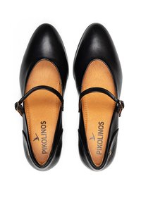 Chaussures Mary Jane en cuir noir avec un bout rond, une sangle réglable et un intérieur beige comportant des détails en relief et un logo au niveau de la semelle.