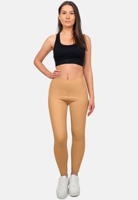 Bra sportivo nero e leggings beige realizzati in tessuto elasticizzato, con vita alta e una texture liscia, abbinati a scarpe da ginnastica bianche.