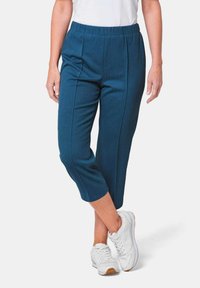 Blauwe, geribbelde, cropped broek met een rekbare tailleband en twee verticale voornaden, gecombineerd met witte sneakers.