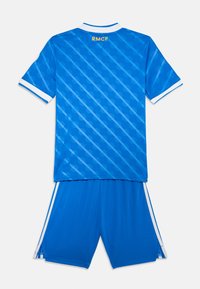 Modrý futbalový dres a šortky so geometrickým vzorom, biele akcenty na golieri a rukávoch, s nápisom "RMCF" v žltej farbe na zadnej strane.