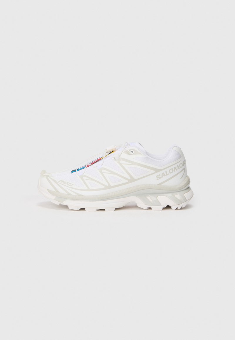 Zapatilla deportiva blanca con parte superior de malla texturizada, acentos reflectantes y suela acolchada. Logotipo de la marca notable en el costado.