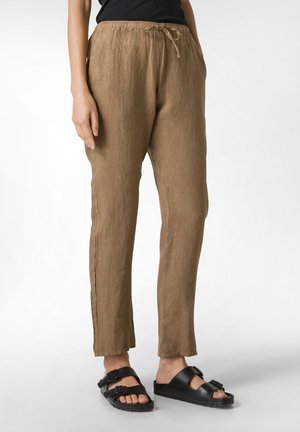 Bruine linnen broek met een elastische tailleband en trekkoord, met een relaxte pasvorm en zijnaad. Gelaagd met zwarte sandalen.