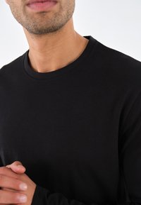 Black long-sleeve crew neck shirt in soft fabric, featuring a plain design with a smooth texture and relaxed fit.