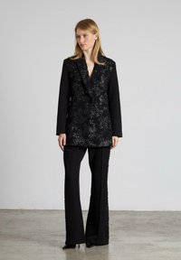 Blazer negro con intrincados bordados florales de lentejuelas, combinado con pantalones negros de corte recto. Tejido suave con un ajuste entallado y solapas afiladas.