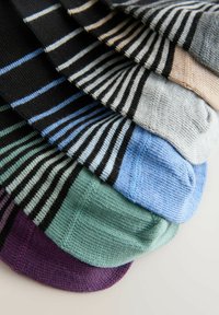 Gestapelter Satz gefalteter, gestreifter Socken in Schwarz-, Beige-, Blau-, Grün- und Violetttönen, auf einer weißen Oberfläche angeordnet.