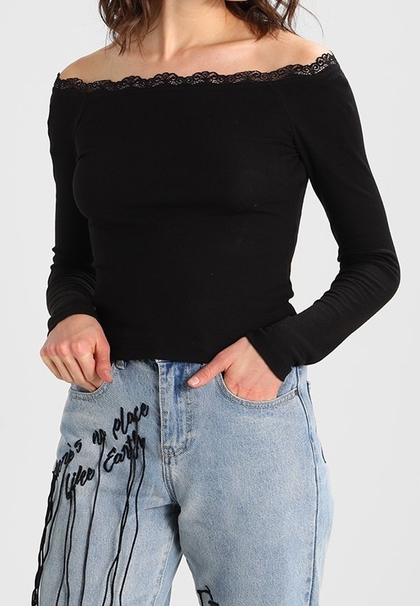 Černý žebrovaný top s dlouhými rukávy, off-the-shoulder výstřihem a krajkovým lemováním, spárovaný se světle modrými džíny s černými grafickými potisky.