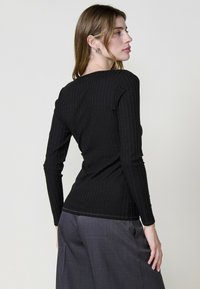 Haut noir à manches longues côtelé avec une silhouette ajustée. Présente un décolleté rond subtil et des coutures nettes. Associé à un pantalon large gris.